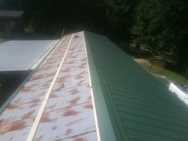 Old rusted panels beside newly installed green metal roofing — Wind Damage Roof Repair by Roofing Brothers in Little Compton