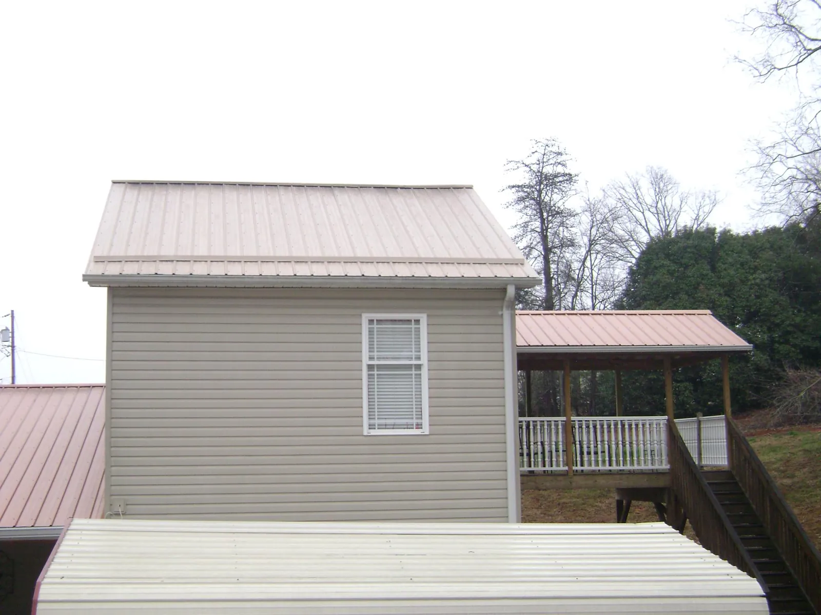 Tan metal roofs on a two story addition and attached porch, from a Roof Replacement job in Little Compton