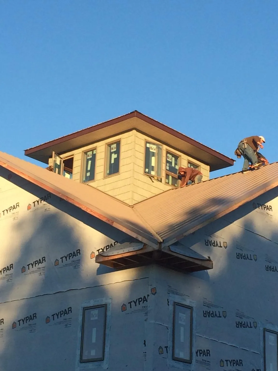 Roofers working around a rooftop cupola on a new metal roof at sunset — Roof Waterproofing in Little Compton by Roofing Brothers